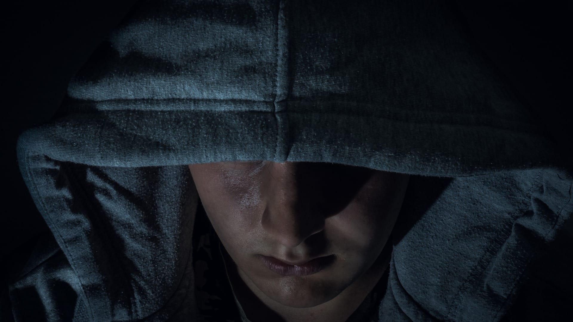 A person with a hood pulled over their head, partially obscuring their face, is shown in low lighting, reminiscent of recent East Cobb home invasions.