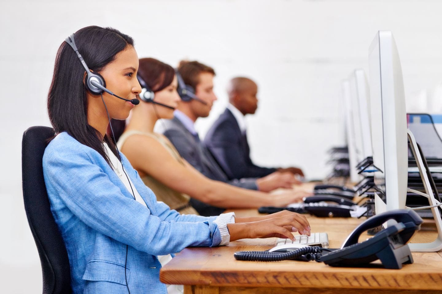 Four people wearing headsets sit at desks working on computers in a row, focusing intently on their screens, resembling the bustling efficiency of Georgia Central Station.