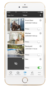 A smartphone displays a security app from New Systems, showing live video feeds from four areas: front door, kitchen, backyard, and den. Privacy settings are available for each feed.