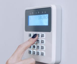 A person is entering numbers on a wall-mounted keypad, likely for home security.