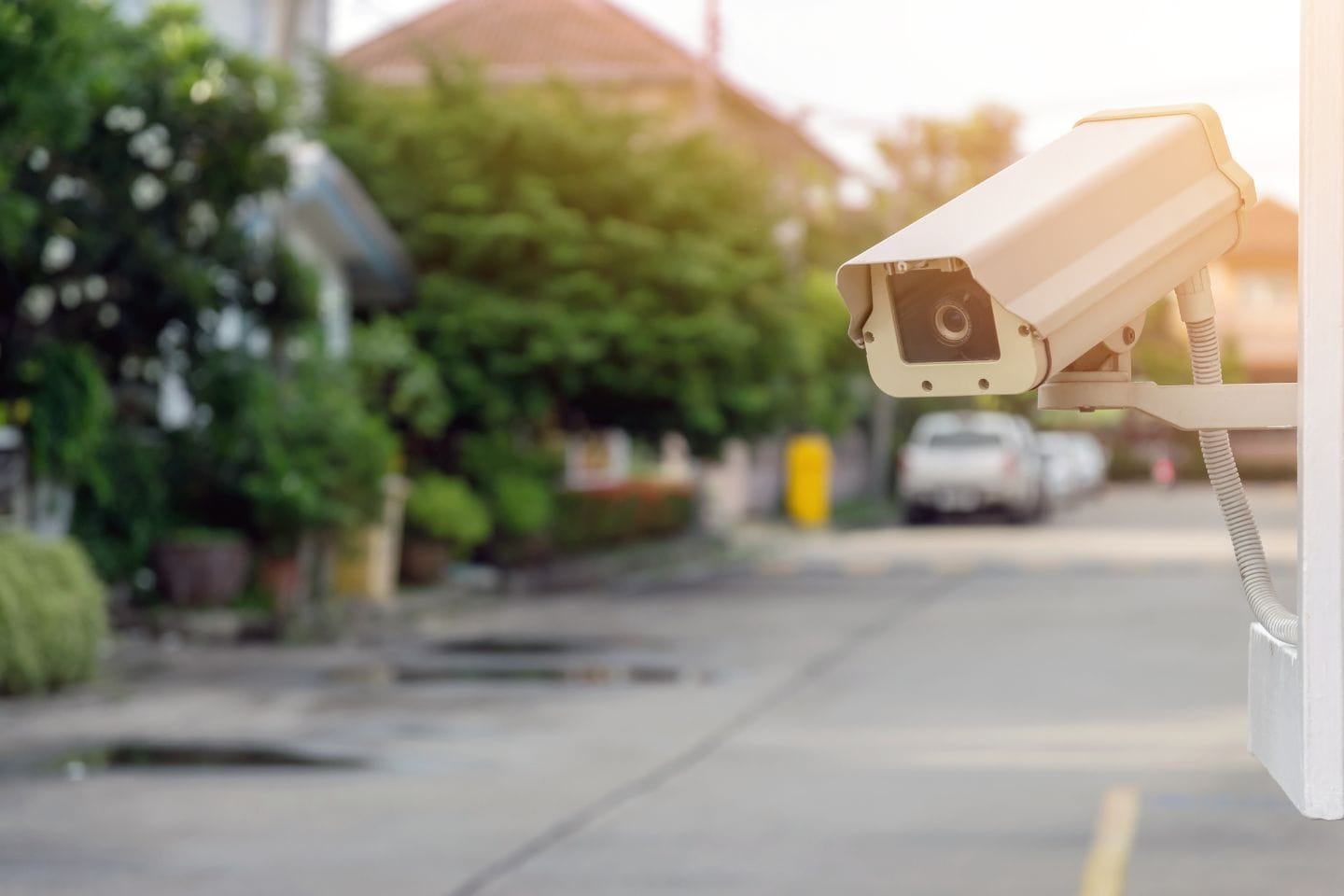 A CCTV system mounted on a white wall overlooks a residential street with houses, cars, and greenery in the background.