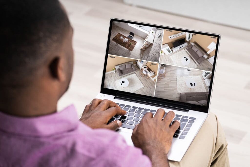 A person wearing a pink shirt reviews four CCTV feeds from a recent security camera installation on a laptop.