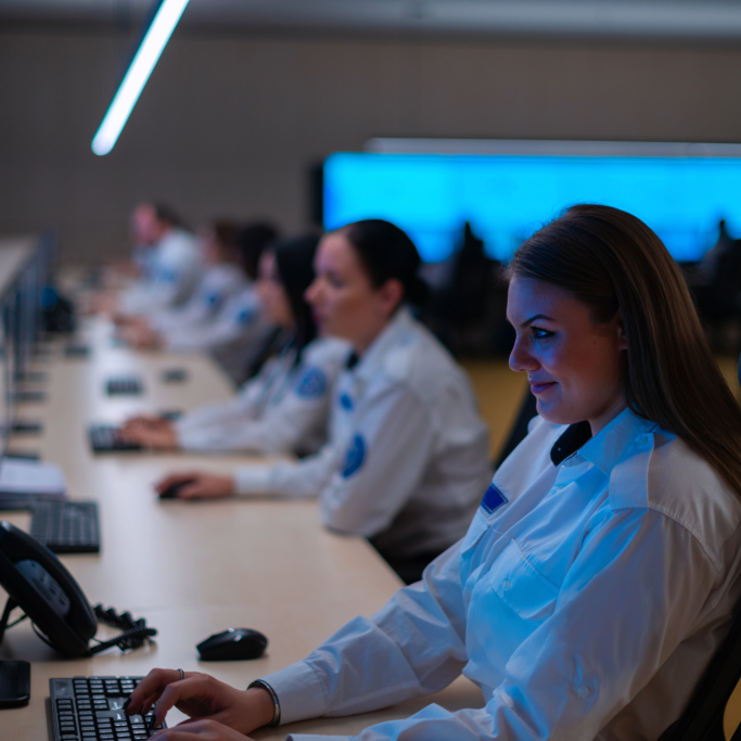 In Georgia's Central Station, people in uniforms sit in a row at computer desks, focused on their screens, in a dimly lit control room with illuminated monitors in the background.