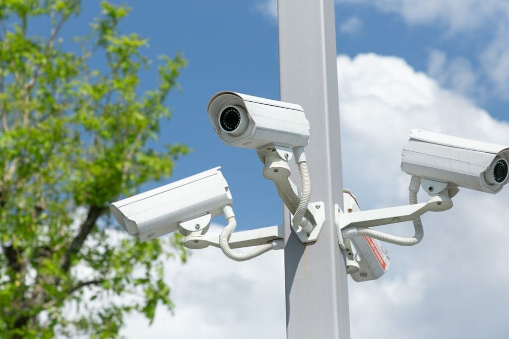 Several security cameras are mounted on a pole with a tree and a cloudy sky in the background, exemplifying the importance of security in any business setting.