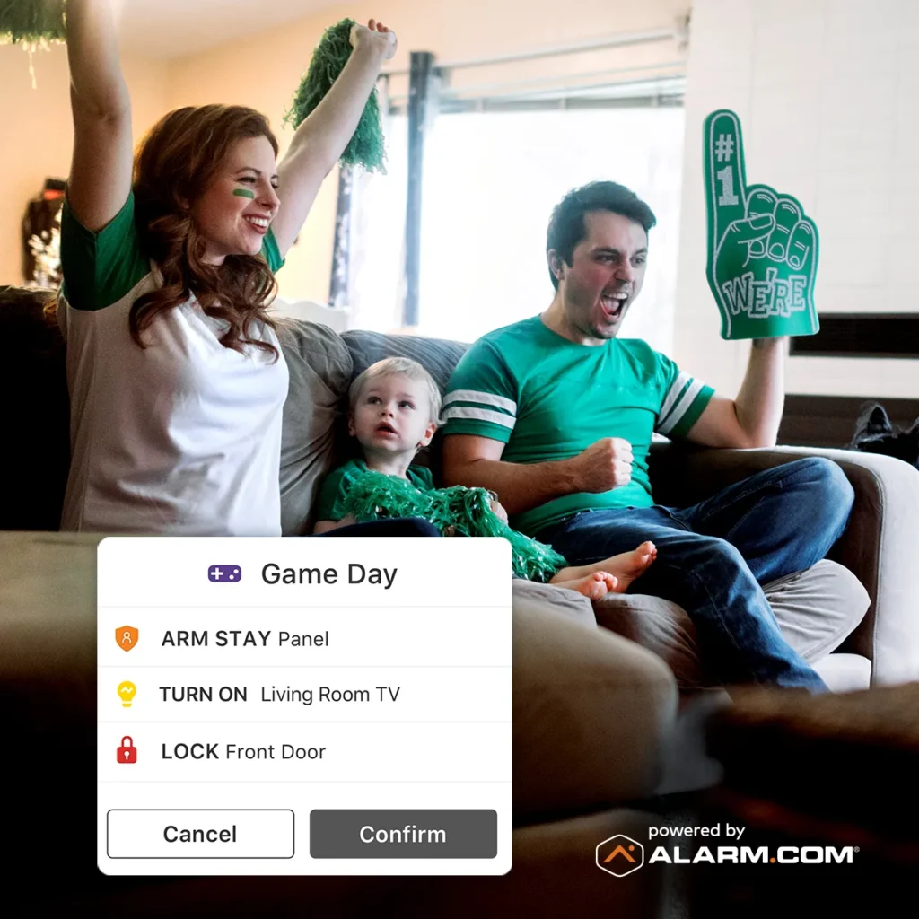 The family is cheering on a cozy couch in their living room, with a pop-up display from Alarm.com showcasing smart home security controls.