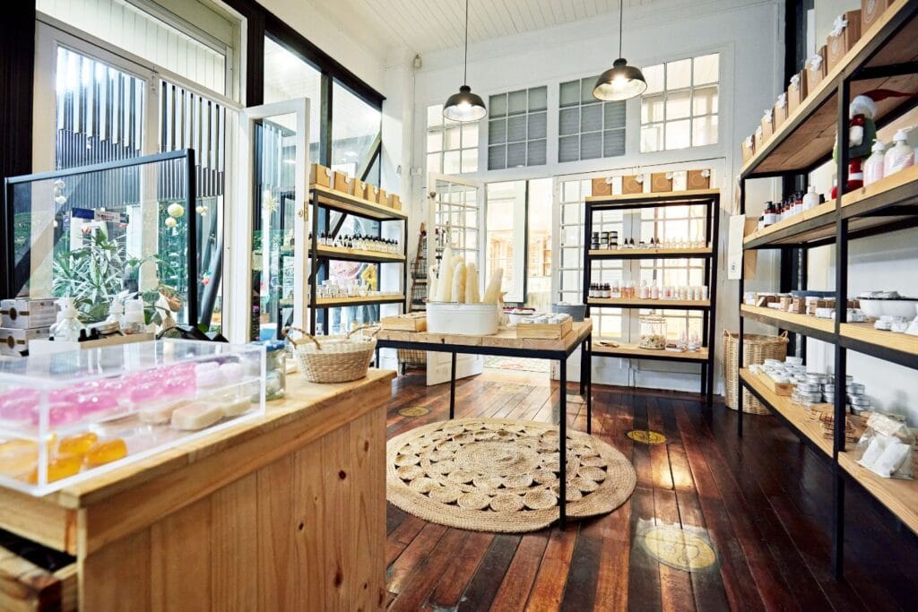 A well-lit shop interior with wooden floors and shelves displaying various goods. Central table holds candles. Glass doors at the back open to an outdoor area, secured by top-tier business security solutions.